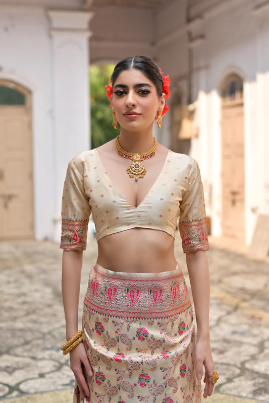 Woman in beige zari work saree with intricate patterns standing in a traditional courtyard