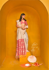 Model wearing beige zari work saree with pink pallu and deep-neck blouse, styled with traditional gold jewellery and seashell decor in yellow arch setting