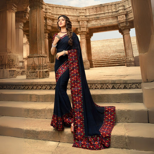 Woman in a black jacquard work saree with gold border standing indoors in an elegant room with arched decor and vintage furniture elements