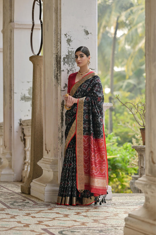 Woman draped in elegant black Pochampali Ikkat saree with zari weaving, styled gracefully on a vintage balcony
