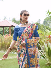 Woman wearing a blue blouse and a vibrant Madhubani-printed saree with multicolor floral and animal motifs, accessorized with traditional jewelry, standing gracefully on a lush green lawn surrounded by tropical plants and red foliage, with a garden gazebo in the background.