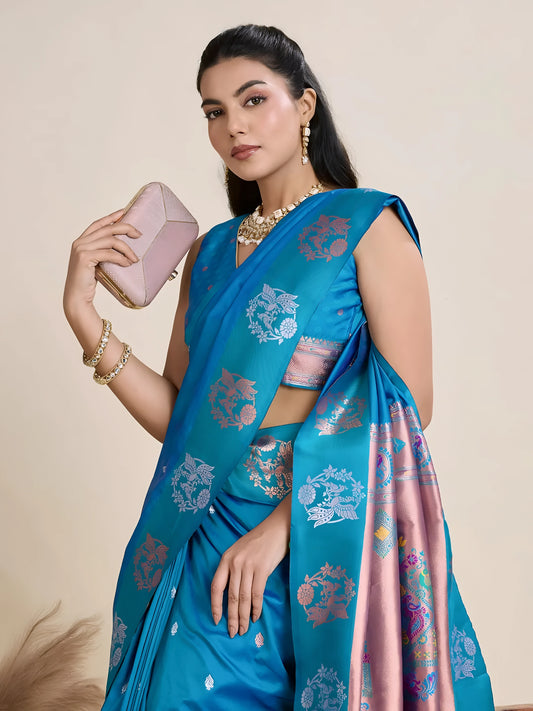 Woman wearing a vibrant blue silk saree with intricate pink and silver woven border and pallu, paired with a matching blouse and gold jewelry, elegantly posing beside a wooden chair in a minimalist studio setting with neutral decor, ceramic vases, and pampas grass.

Related
blue-silk-saree-pink-border-modern-studio
Woman in a vibrant blue silk saree with pink border and intricate details in a modern studio setting.
