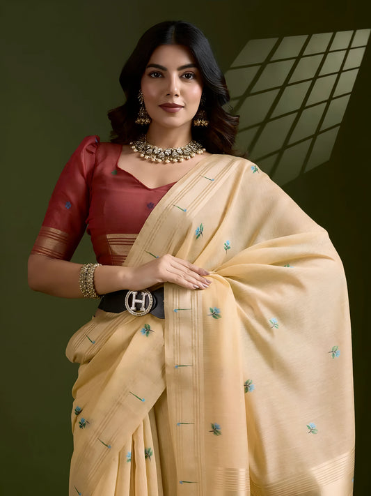  Woman wearing a cream silk saree adorned with delicate floral embroidery and tassel detailing on the pallu, paired with a red blouse and traditional jewelry, elegantly posing in a contemporary studio with olive green walls and decorative window light patterns.