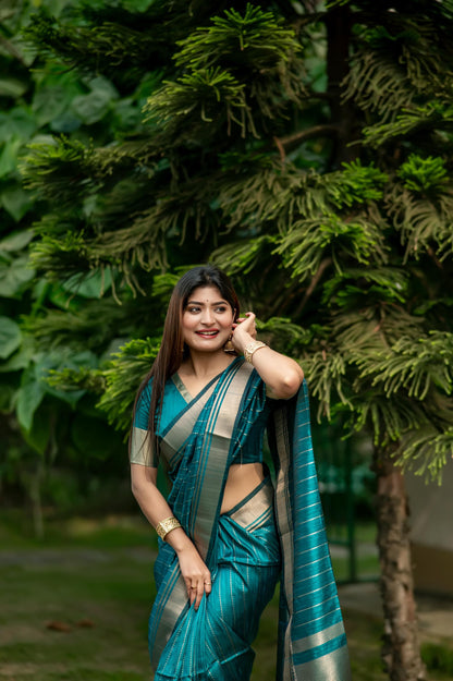 Woman in a dark green saree with zari work standing on a garden pathway surrounded by lush greenery