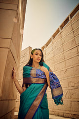 Elegant woman draped in deep green saree with rich zari work and intricate pallu design, posing against contemporary sandstone architecture