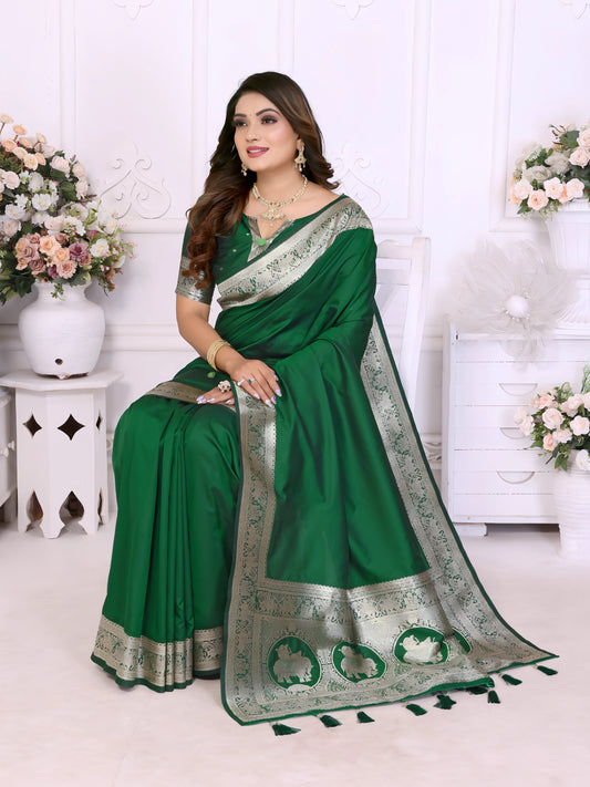Woman wearing an elegant emerald green silk saree with a rich silver zari border and matching blouse, posing gracefully in a white floral-themed room with classic wall panels and decorative flower arrangements.