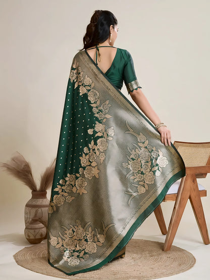 Woman wearing a green Banarasi silk saree with intricate gold floral zari border and pallu, paired with a matching blouse and traditional jewelry, elegantly posing beside a wooden chair in a minimalist studio with neutral decor, ceramic vases, and pampas grass.