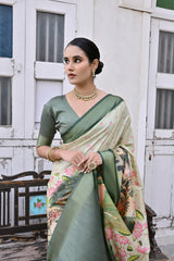  Woman wearing a green floral saree with intricate patterns and a matching green blouse, accessorized with traditional gold jewelry including a statement necklace, standing beside a vintage wooden bench in front of weathered white doors with green and blue stained glass panels in a heritage-style courtyard setting.