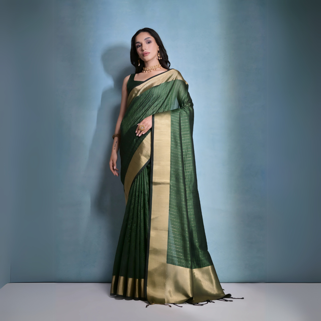 Woman wearing a green silk saree with gold border and traditional jewelry, posing against a plain blue background