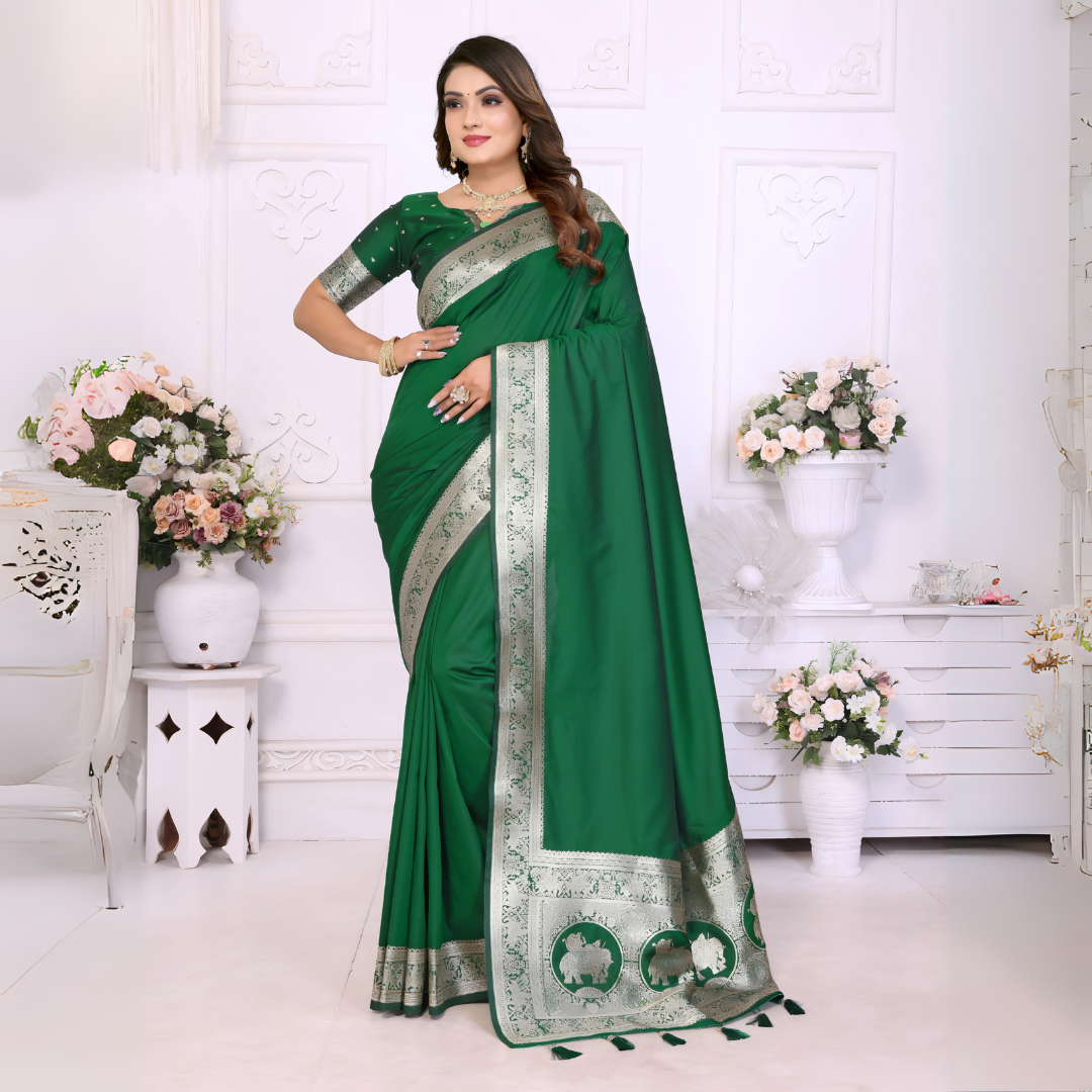 Woman wearing an elegant emerald green silk saree with a rich silver zari border and matching blouse, posing gracefully in a white floral-themed room with classic wall panels and decorative flower arrangements.