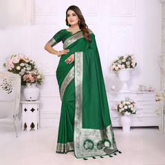 Woman wearing an elegant emerald green silk saree with a rich silver zari border and matching blouse, posing gracefully in a white floral-themed room with classic wall panels and decorative flower arrangements.