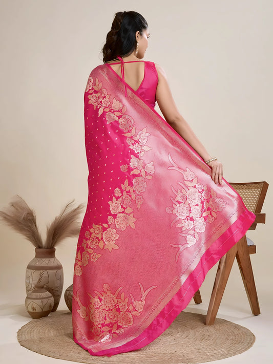 Woman wearing a hot pink Banarasi silk saree with intricate gold floral zari border and pallu, paired with a matching blouse and traditional jewelry, elegantly posing beside a wooden chair in a minimalist studio with neutral decor, ceramic vases, and pampas grass.