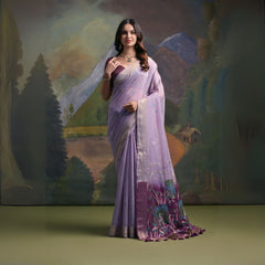 Woman wearing a lavender silk saree with intricate peacock embroidery and floral motifs on the pallu, paired with a matching blouse and traditional jewelry, standing in front of a painted mountain and forest backdrop.