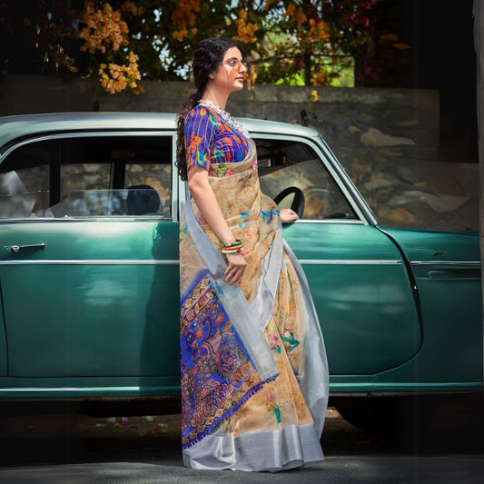 Woman in a light beige floral print saree standing beside a vintage car with colorful flowers in the background
