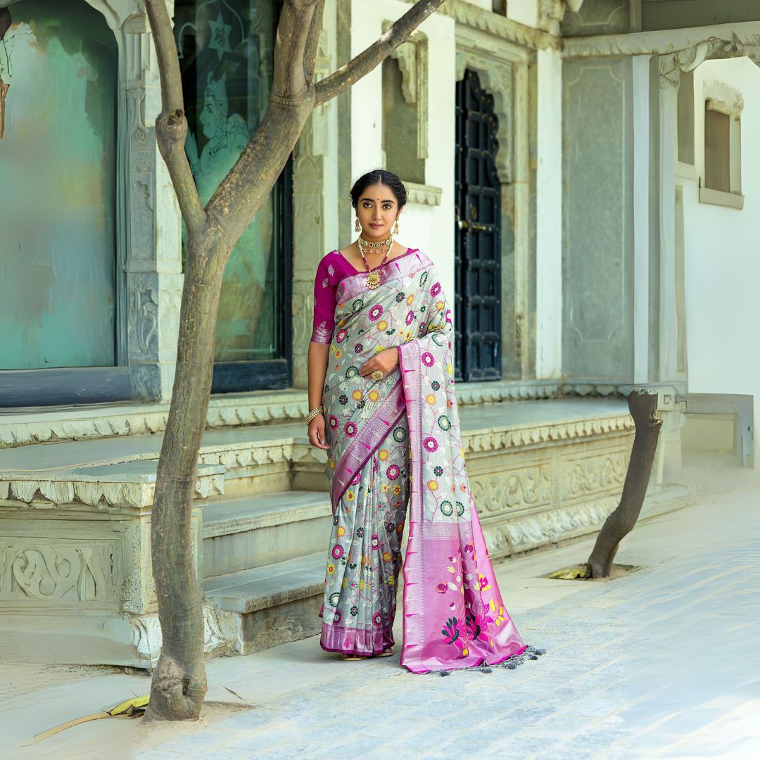 Woman wearing light gray saree with intricate zari work and pink blouse in traditional Indian setting