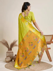 Woman wearing a lime green silk saree with gold motifs and matching blouse, accessorized with a pearl choker necklace and bangles, elegantly posing beside a wooden chair in a minimalist studio setting with neutral decor, ceramic vases, and pampas grass.