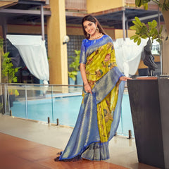 Woman wearing a lime zari work saree with a blue pallu and floral design, styled with gold jewelry and a modern traditional look by the poolside