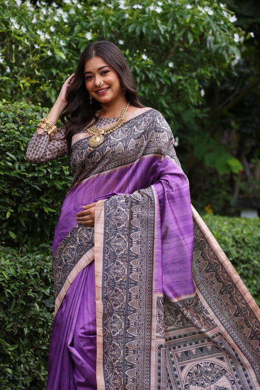 Woman wearing traditional purple Madhubani print saree with intricate designs and ethnic jewelry in a green outdoor setting
