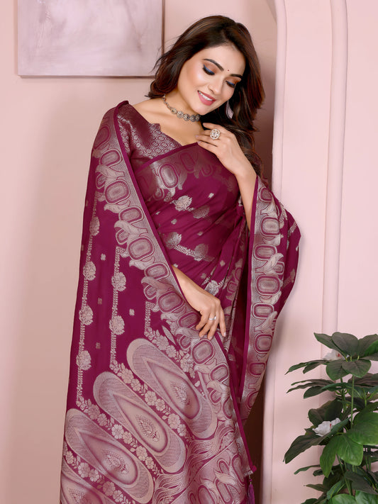 Woman wearing a magenta Banarasi saree with intricate silver zari motifs and rich ethnic border, paired with a matching silver blouse with short sleeves. She poses gracefully in an elegant arched pastel setting with minimal decor, including a white pedestal with vases and a potted green plant, showcasing a traditional Indian festive look.