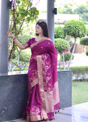 Woman wearing a magenta saree with beige floral embroidery and border, posing outdoors near green landscaped bushes and trees.