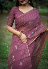 Woman in magenta traditional weaving saree with delicate motifs posing gracefully in a natural outdoor setting.