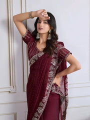 Woman wearing a maroon georgette saree adorned with delicate sequins and an ornate silver embroidered border, paired with a matching blouse and traditional jhumka earrings. She stands elegantly in a classic white paneled room with a vintage rotary telephone on a carved wooden side table, a modern wooden chair with a woven seat, and a patterned rug, creating a sophisticated and timeless ambiance.