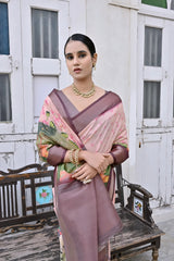 Woman wearing a mauve floral silk saree with a contrasting border and traditional jewelry, elegantly standing beside a vintage wooden bench in front of classic white arched doors and windows, with greenery on the side in a heritage courtyard setting.