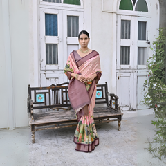 Woman wearing a mauve floral silk saree with a contrasting border and traditional jewelry, elegantly standing beside a vintage wooden bench in front of classic white arched doors and windows, with greenery on the side in a heritage courtyard setting.