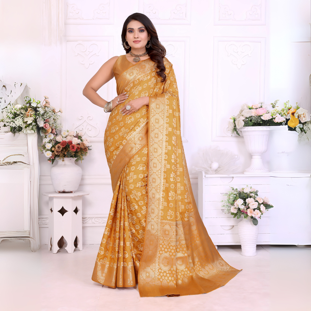 Woman wearing a mustard yellow Banarasi silk saree featuring intricate gold traditional motifs and a shimmering woven border, paired with a matching blouse and statement jewelry. She poses elegantly in a classic white room adorned with ornate wall panels and decorative vases overflowing with pastel and white artificial flowers.