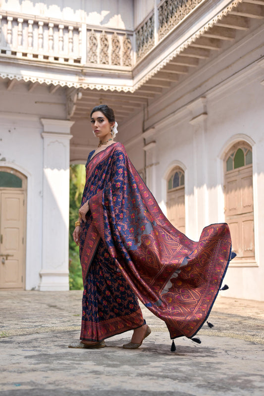 Woman in navy blue zari work saree with intricate patterns in a traditional courtyard setting
