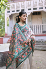 Woman wearing an off-white silk saree with green Patola-inspired geometric and floral borders, featuring intricate floral motifs, paired with traditional jewelry, elegantly posing on stone steps in front of a vintage heritage house with ornate wooden railings and lush greenery in the background.