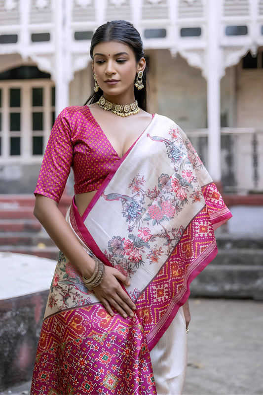 Woman wearing an off-white silk saree with vibrant pink Patola-inspired geometric and floral borders, featuring intricate floral motifs, paired with a matching pink blouse and traditional jewelry, elegantly posing on stone steps in front of a vintage heritage house with ornate railings and classic architectural details.