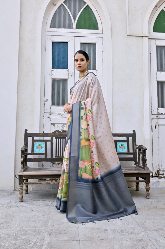 Woman wearing a pastel floral silk saree with a grey border and matching grey blouse, accessorized with traditional gold jewelry, elegantly standing in front of classic white arched doors and windows beside a vintage wooden bench, with greenery and a floral arrangement in a heritage courtyard setting.