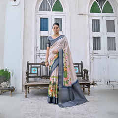 Woman wearing a pastel floral silk saree with a grey border and matching grey blouse, accessorized with traditional gold jewelry, elegantly standing in front of classic white arched doors and windows beside a vintage wooden bench, with greenery and a floral arrangement in a heritage courtyard setting.