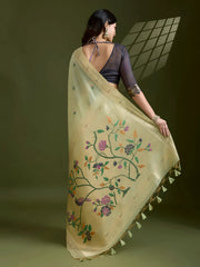 Woman wearing a pastel green silk saree with subtle embroidered motifs and golden zari border, paired with a black three-quarter sleeve blouse and traditional jewelry, elegantly posing in a contemporary studio with olive green walls and artistic window light patterns.