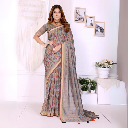 Woman wearing a pastel grey handloom saree featuring subtle multicolor geometric patterns and a beige border, styled with a matching blouse and traditional jewelry including a choker necklace and bangles. She poses elegantly in a modern room with white walls, macramé wall hanging, minimalist picture frames, and potted plants on white platforms, creating a refined and contemporary setting.