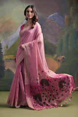 Woman wearing a pastel pink silk saree with delicate floral embroidery and a contrasting pink blouse, standing gracefully in front of a painted mountain and forest backdrop, accessorized with traditional jewelry.