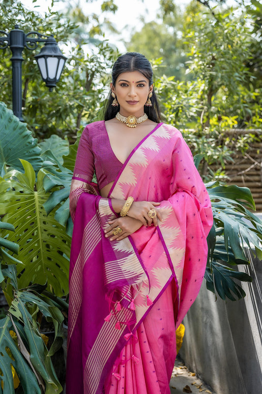 A woman models a vibrant Hot Pink Tussar Silk Saree with small woven motifs. The saree has a gold temple border, and the pallu features wide bands of deep magenta and gold Zari weaving. She wears a magenta blouse and heavy gold Kundan jewelry.