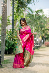 Woman wearing a vibrant pink zari work saree and gold jewelry smiling outdoors in a lush garden setting