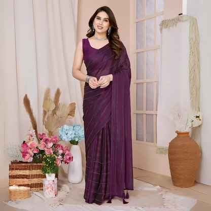 Woman wearing a plum-colored saree with subtle sequin stripes and a sleeveless blouse, accessorized with silver jewelry, standing in a modern interior decorated with vases of pink and blue flowers, a wicker basket, and neutral decor elementsWoman wearing a plum-colored saree with subtle sequin stripes and a sleeveless blouse, accessorized with silver jewelry, standing in a modern interior decorated with vases of pink and blue flowers, a wicker basket, and neutral decor elements