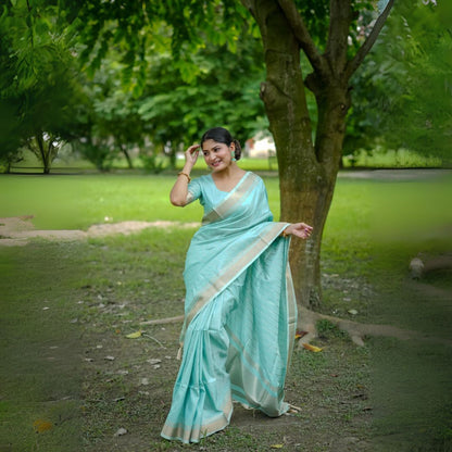 Woman in a powder blue saree with zari work posing in a park near a tree