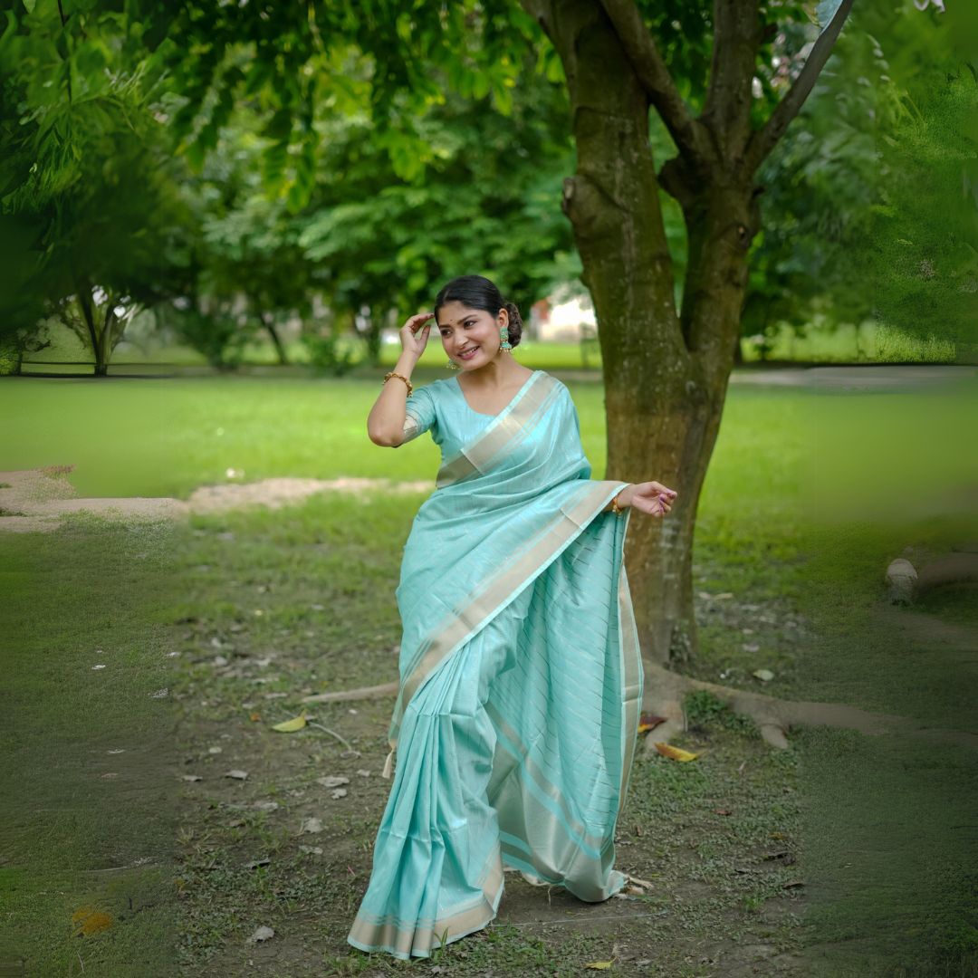 Woman in a powder blue saree with zari work posing in a park near a tree