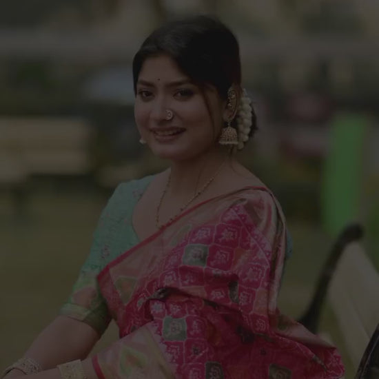 Woman wearing a red blouse and a saree with pink and green floral zari work. 