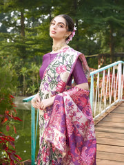 Woman wearing a purple saree with vibrant Madhubani-inspired floral print border and pallu, paired with a matching blouse and traditional jewelry, gracefully standing on stone steps beside a wooden bridge surrounded by lush greenery and colorful garden plants.