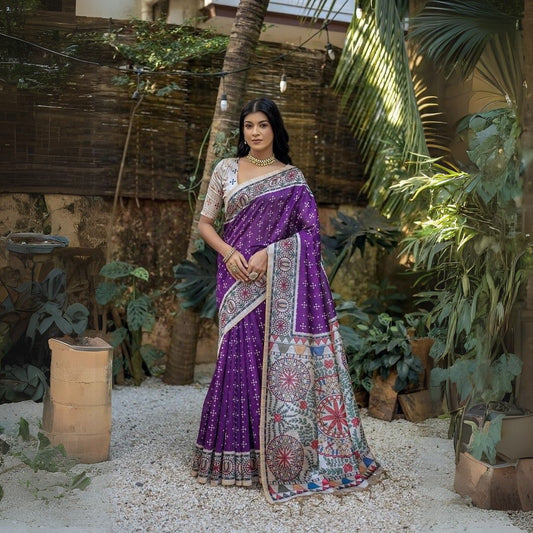 A woman models a Royal Purple Tussar Silk Saree with small white scattered prints. The pallu features a wide, elaborate panel with intricate Madhubani-style folk art prints in white, red, green, and blue. She wears a cream/gold embellished blouse and a gold Kundan choker necklace.