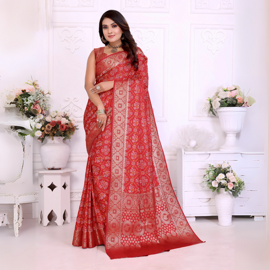 Woman draped in a vibrant red Banarasi bandhani saree featuring intricate white tie-dye patterns and an ornate zari border, paired with a matching sleeveless blouse and silver jewelry. She poses elegantly in a classic white room decorated with decorative wall panels and lush flower arrangements in white vases.