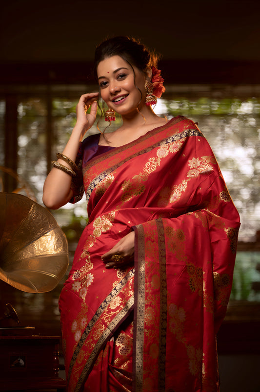Woman wearing a red Banarasi silk saree with intricate gold zari border and floral motifs, accessorized with traditional jewelry, standing in a vintage-inspired room with checkered flooring, a gramophone, floral decor, and bamboo blinds filtering natural light.
