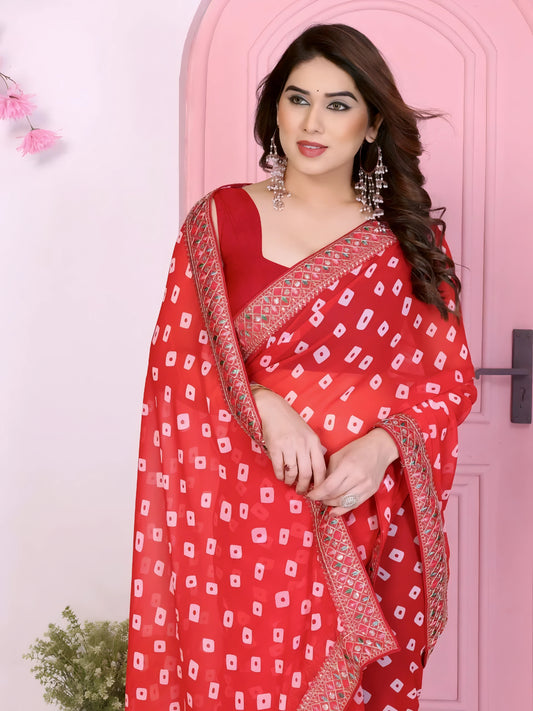 Woman wearing a vibrant red bandhani saree adorned with traditional white tie-dye patterns and a gold embroidered border, paired with a matching sleeveless blouse and accessorized with statement earrings and bangles. She stands gracefully in front of a pastel pink arched doorway, surrounded by earthy clay pots, a green foliage vase, and decorative pink branches in a modern studio setting.