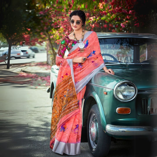 Woman in a soft peach floral print saree leaning against a vintage car with scattered petals and vibrant flowers in the background