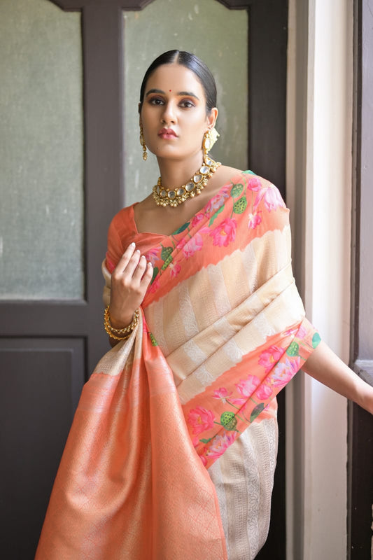 Beautiful Indian woman in a soft peach zari work silk saree, adorned with traditional jewelry, standing by a window.